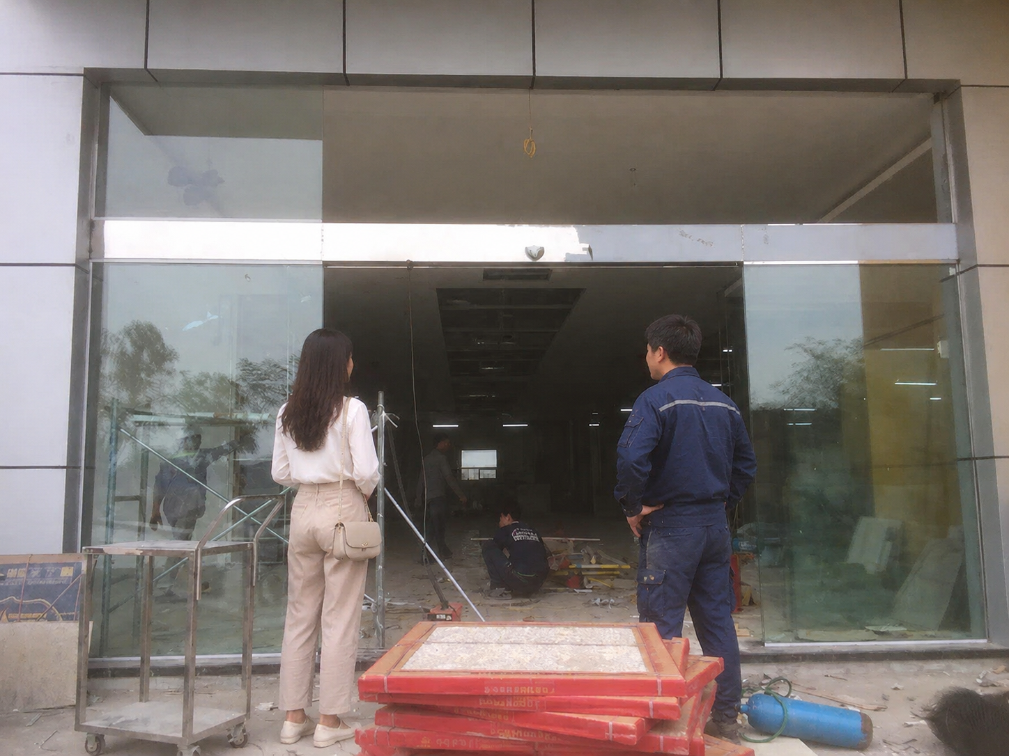 Cửa kính cường lực mặt tiền tòa nhà đang thi công với thợ lắp đặt và khách hàng đứng quan sát